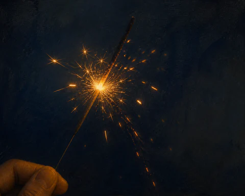 A single sparkler burns and decays into amber trails against deep indigo darkness
